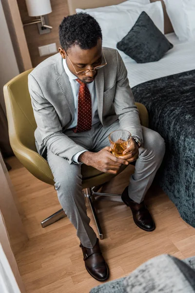 Homme américain africain déprimé tenant un verre de whisky dans la chambre d'hôtel — Photo de stock