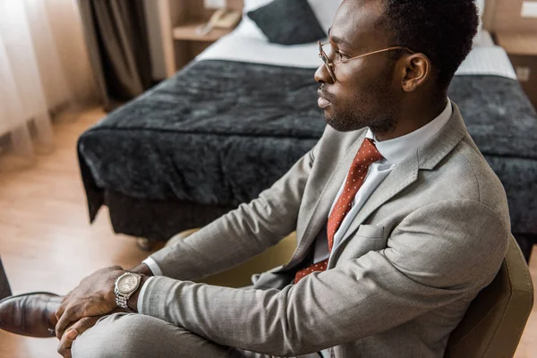 Pensive african american businessman in gray suit sitting in hotel room — Stock Photo