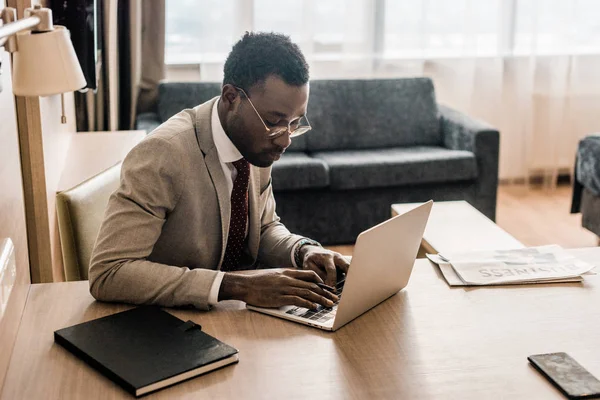 Hombre de negocios afroamericano que trabaja en el ordenador portátil en la habitación de hotel - foto de stock