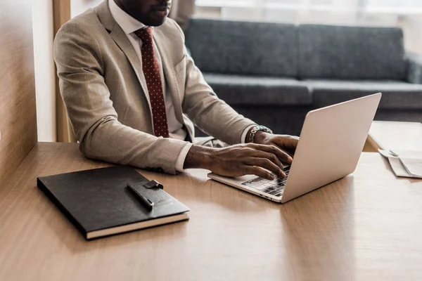 Обрезанный вид африканского американского бизнесмена, работающего на ноутбуке в гостиничном номере — стоковое фото