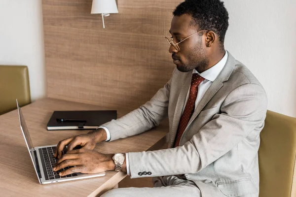 Homme d'affaires afro-américain concentré tapant sur ordinateur portable dans la chambre d'hôtel — Photo de stock