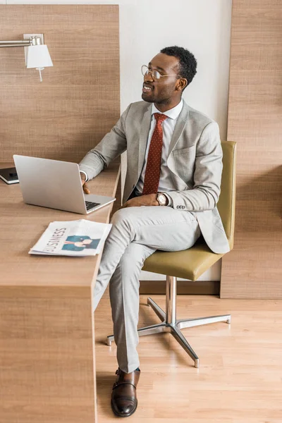 Homme d'affaires afro-américain travaillant sur ordinateur portable dans la chambre d'hôtel avec journal — Photo de stock