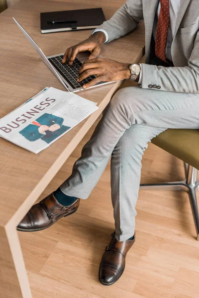 Cropped view of african american businessman using laptop in hotel with business newspaper — Stock Photo