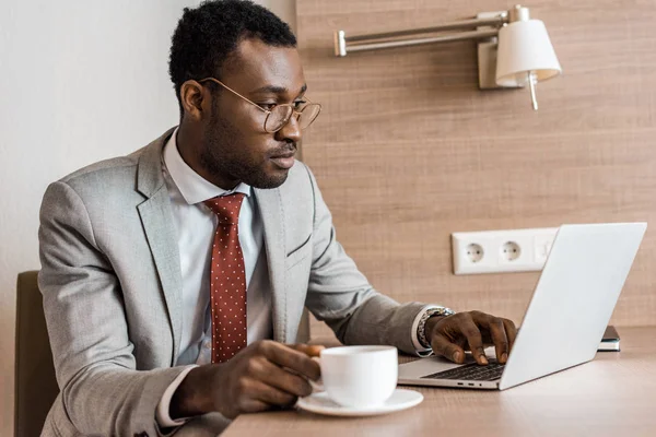 Африканский американский бизнесмен с кофе работает на ноутбуке в гостиничном номере — стоковое фото