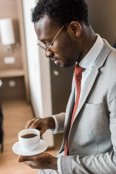 Afrikanisch-amerikanischer Geschäftsmann blickt auf Tasse Kaffee im Hotelzimmer — Stockfoto