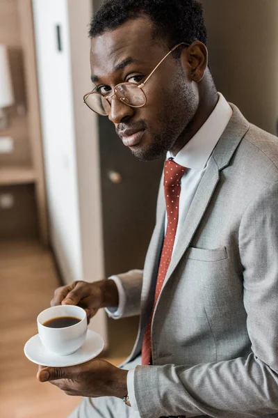 Bonito Africano americano empresário segurando xícara de café no quarto de hotel — Fotografia de Stock