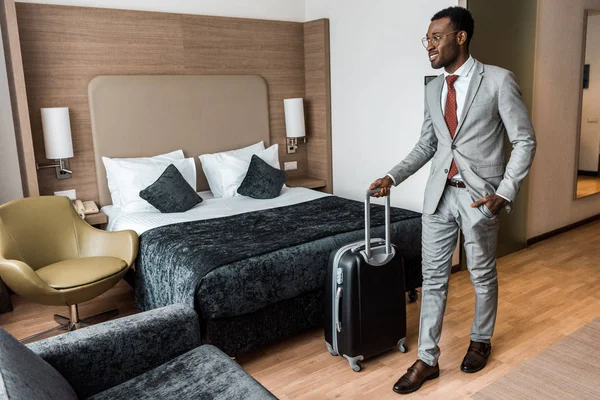 Sonriente hombre de negocios afroamericano con bolsa de viaje en habitación de hotel - foto de stock