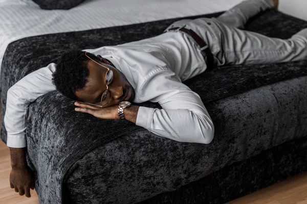 Hombre afroamericano agotado en ropa formal durmiendo en la cama en la habitación de hotel - foto de stock