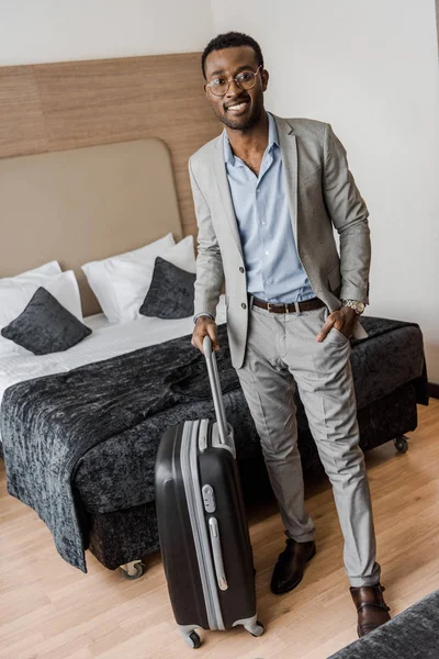 African american businessman in suit with suitcase in hotel room with bed — Stock Photo