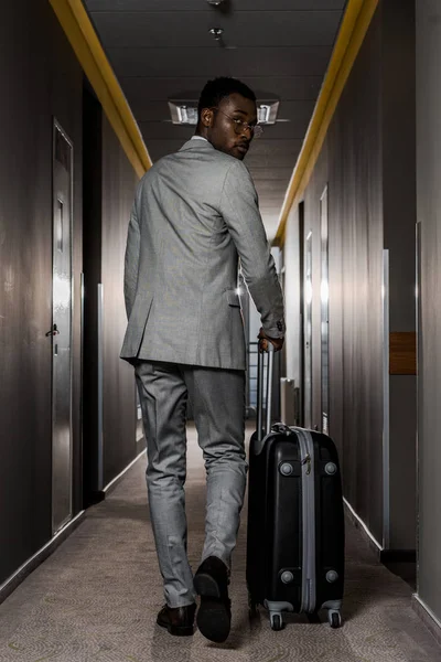 Vue arrière de l'homme d'affaires afro-américain avec bagages marchant dans le couloir de l'hôtel — Photo de stock