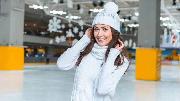 Portrait de belle femme souriante en chapeau et pull regardant la caméra sur la patinoire — Photo de stock
