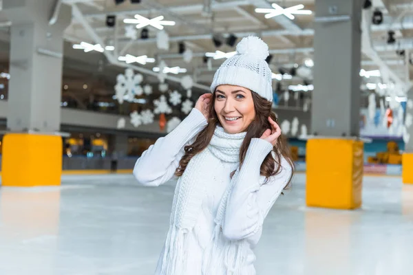 Porträt einer lächelnden schönen Frau mit Hut und Pullover, die auf der Eisbahn in die Kamera blickt — Stockfoto