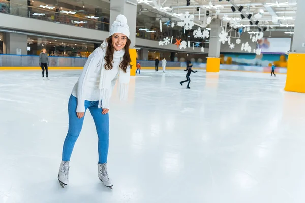 Lächelnde junge attraktive Frau im Strickpullover läuft allein auf der Eisbahn Schlittschuh — Stockfoto