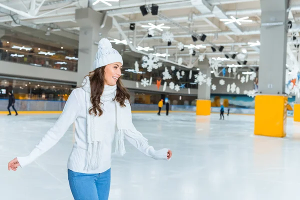 Lächelnde junge attraktive Frau im Strickpullover läuft allein auf der Eisbahn Schlittschuh — Stockfoto