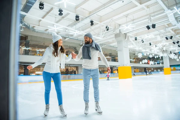 Happy couple holding hands while skating on rink together — Stock Photo