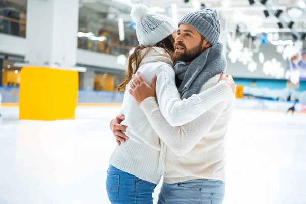 Seitenansicht eines verliebten Paares, das sich beim gemeinsamen Schlittschuhlaufen auf der Eisbahn umarmt — Stockfoto