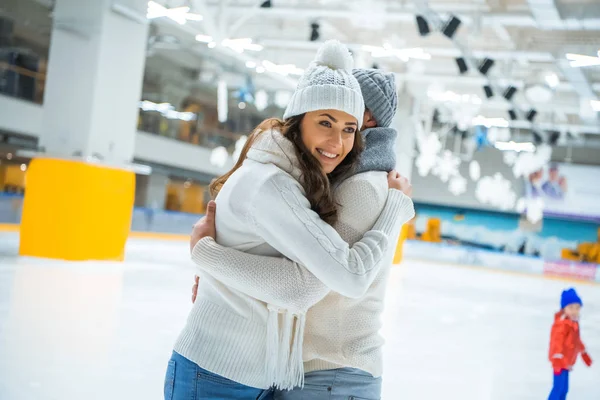Vista lateral de pareja enamorada abrazándose mientras patinan juntos en pista de hielo - foto de stock