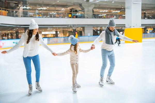 Family in sweaters holding hands while skating together on ice rink — Stock Photo