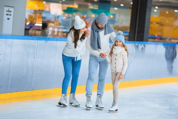 Padres sonrientes mirando a su hija mientras patinan juntos en la pista de patinaje - foto de stock