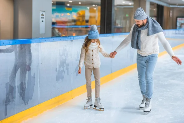 Father and daughter in knitted sweaters skating on ice rink together — Stock Photo