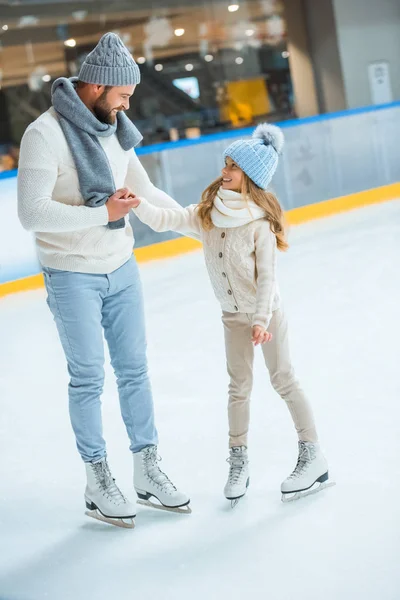 Sonrientes padre e hija mirándose en la pista de patinaje - foto de stock