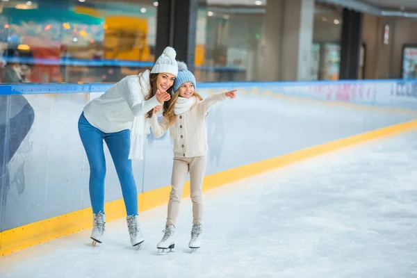 Lächelnde Mutter und Tochter zeigen auf Eisbahn — Stockfoto