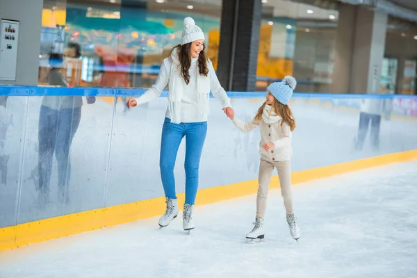 Lächelnde Mutter und Tochter halten sich Händchen und laufen gemeinsam auf der Eisbahn — Stockfoto