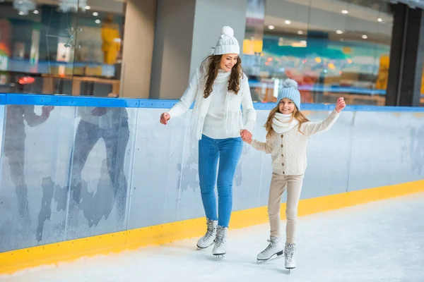 Lächelnde Mutter und Tochter halten sich Händchen und laufen gemeinsam auf der Eisbahn — Stockfoto