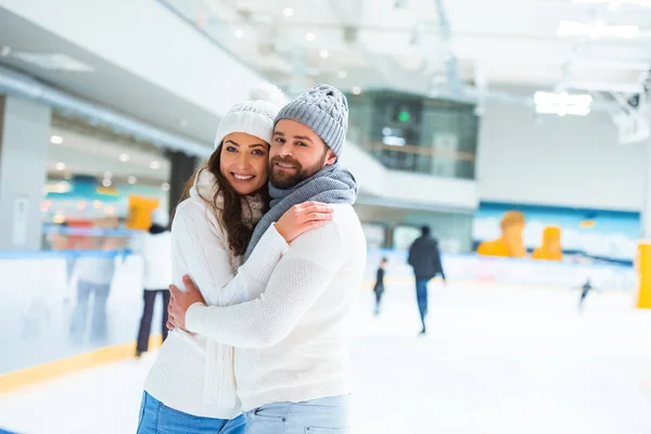 Retrato de pareja feliz mirando la cámara mientras se abraza en la pista de patinaje - foto de stock