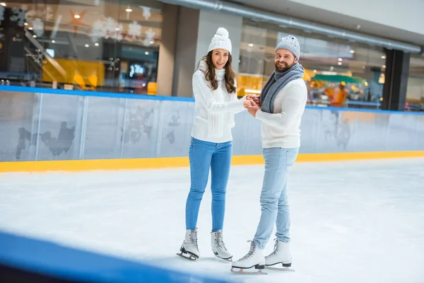 Couple souriant en bonnets et pulls tricotés sur patinoire — Photo de stock