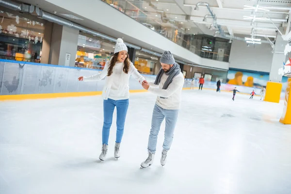 Homem ensinando namorada como patinar na pista de gelo — Fotografia de Stock