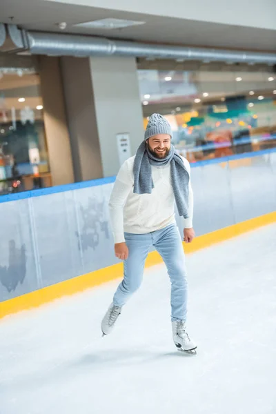 Bearded man in knitted hat and sweater skating on ice rink — Stock Photo