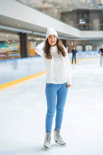 Sonriente joven atractiva mujer en punto suéter patinaje en pista de hielo solo - foto de stock