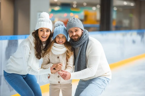 Retrato de pais sorridentes e filha em suéteres olhando para a câmera na pista de patinação — Fotografia de Stock