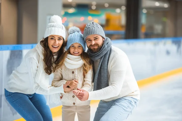Retrato de padres sonrientes e hija en suéteres mirando la cámara en la pista de patinaje - foto de stock