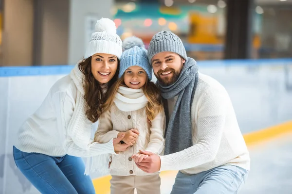 Retrato de padres alegres e hija en suéteres mirando la cámara en la pista de patinaje - foto de stock