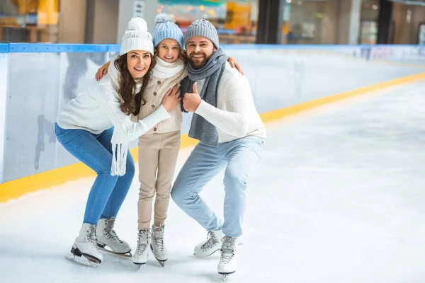 Smiling parents and daughter in sweaters looking at camera on skating rink — Stock Photo