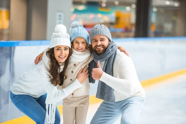 Genitori sorridenti e figlia in maglioni guardando la fotocamera sulla pista di pattinaggio — Foto stock