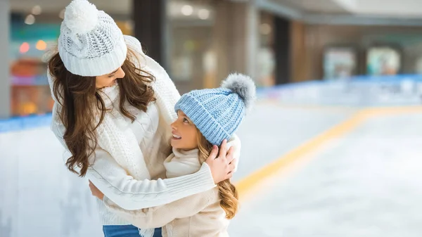 Portrait of mother and daughter hugging each other while skating on ice rink together — Stock Photo