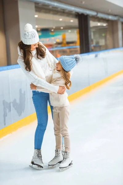 Mãe e filha abraçando um ao outro enquanto patinavam na pista de gelo juntos — Fotografia de Stock