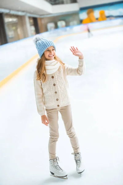 Cheerful kid in sweater and skates greeting someone on skating rink — Stock Photo