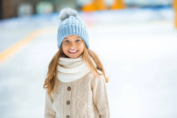 Porträt eines glücklichen Kindes mit Strickmütze, das auf der Eisbahn in die Kamera blickt — Stockfoto