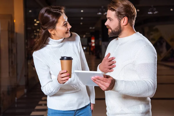 Пара в белых вязаных свитерах глядя друг на друга, используя цифровой планшет вместе — стоковое фото