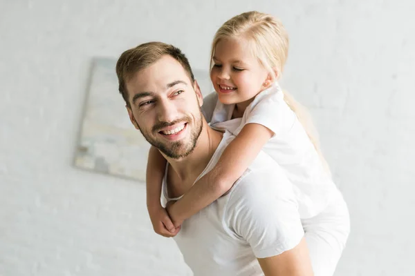 Glücklicher Vater und entzückende kleine Tochter huckepack und Spaß zu Hause — Stockfoto