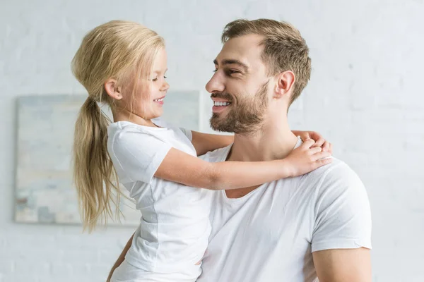 Feliz padre y linda hijita abrazándose y sonriendo en casa - foto de stock