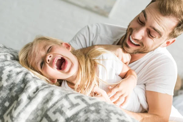 Glücklicher Vater kitzelt süße kleine Tochter und hat Spaß zusammen im Bett — Stockfoto