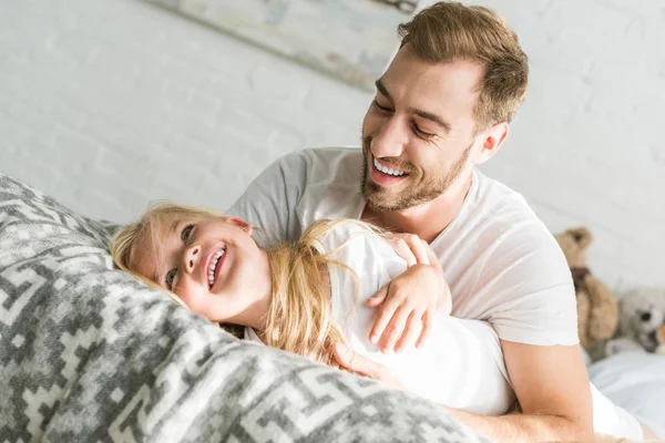 Glücklicher Vater umarmt entzückende kleine Tochter auf dem Bett — Stockfoto