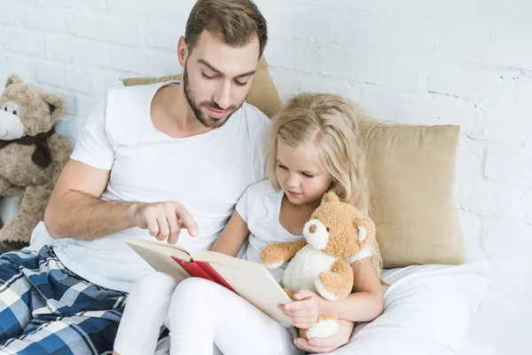 Высокий угол зрения отца и очаровательная маленькая дочь чтение книги вместе на кровати — стоковое фото