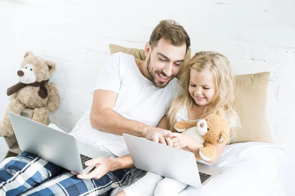 Pai feliz e filha usando laptops na cama — Fotografia de Stock