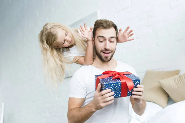 Entzückende kleine Tochter schaut überraschten Vater an, der Geschenkbox zu Hause hält — Stockfoto